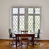 Wohnzimmer in der Villa Rhodius mit Tisch, Sesseln und einem alten Holzfenster