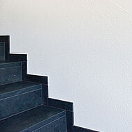 Treppe in einem Treppenhaus vor einer Wand mit Oberputz als Scheibenputz ausgeführt